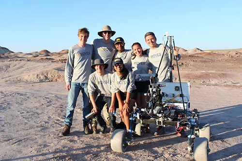 group of students hudle around the Michigan Mars Rover in the desert